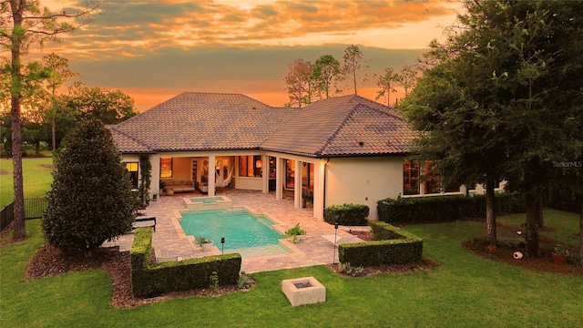 rear view of property featuring a tile roof, stucco siding, a lawn, a patio area, and fence