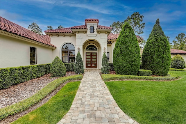 entrance to property featuring french doors, a yard, a tiled roof, and stucco siding