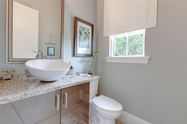 half bath featuring baseboards, vanity, and toilet