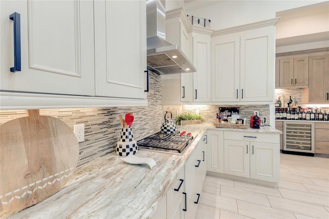 kitchen with light stone counters, beverage cooler, decorative backsplash, wall chimney exhaust hood, and stainless steel gas stovetop