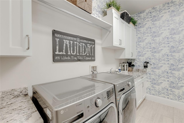 washroom featuring wallpapered walls, washer and clothes dryer, cabinet space, and baseboards