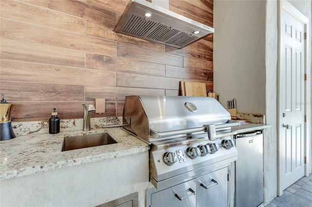 kitchen featuring freestanding refrigerator, a sink, wood walls, ventilation hood, and light stone countertops