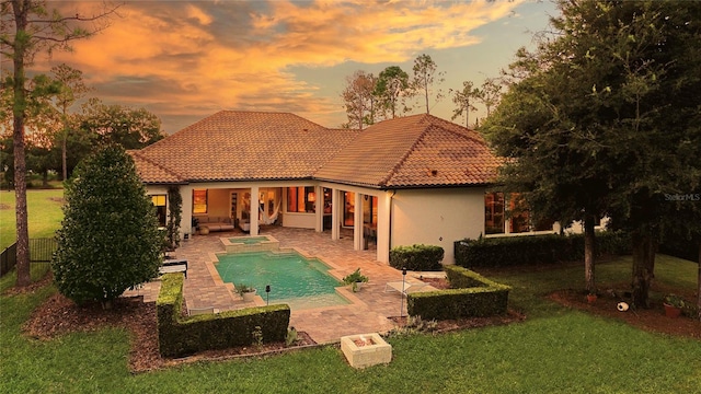 rear view of house with a tile roof, a yard, stucco siding, an outdoor pool, and a patio area