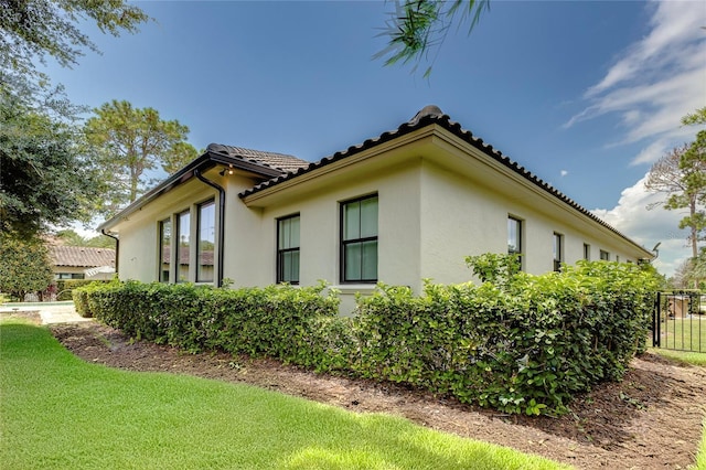 view of side of home with a yard, a tile roof, fence, and stucco siding