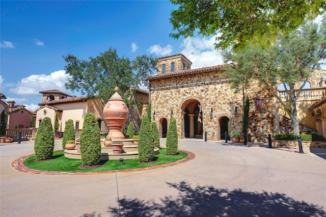 mediterranean / spanish-style home featuring stone siding, curved driveway, and a tiled roof