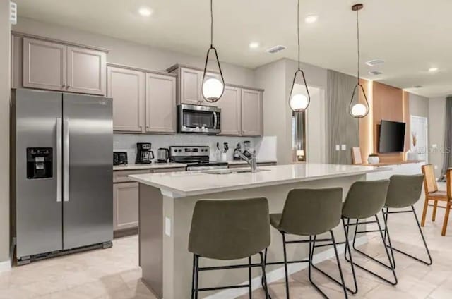 kitchen featuring a kitchen breakfast bar, hanging light fixtures, an island with sink, light tile patterned floors, and stainless steel appliances