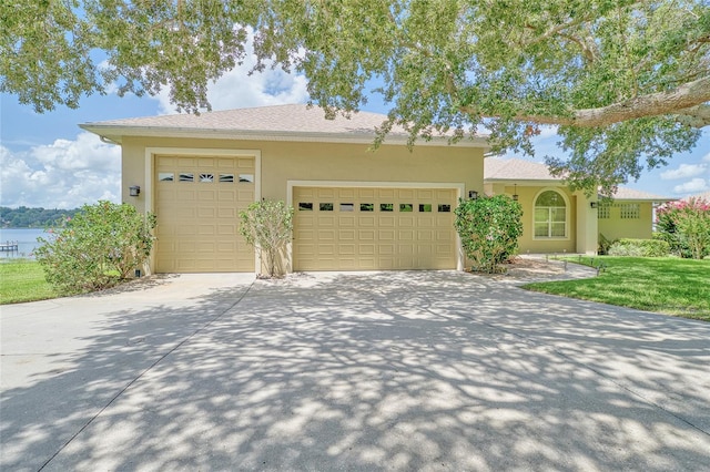 view of front facade with a garage, driveway, a water view, and stucco siding