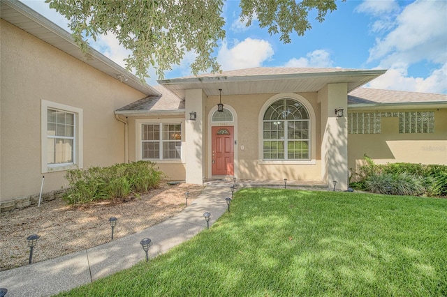 entrance to property with a yard, a shingled roof, and stucco siding