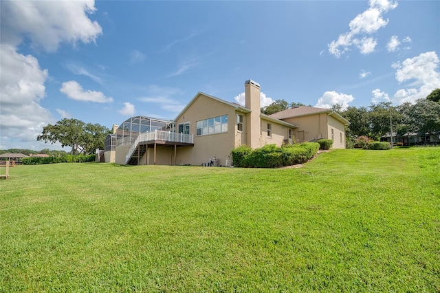 back of property featuring glass enclosure, stairway, a lawn, stucco siding, and a chimney