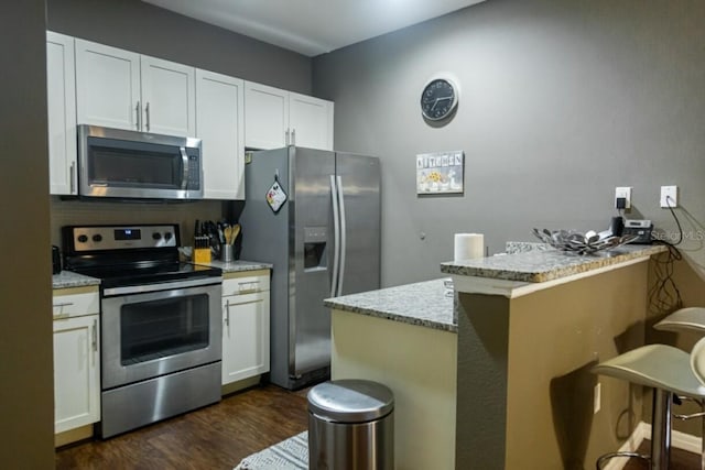 kitchen featuring dark hardwood / wood-style floors, white cabinets, light stone countertops, kitchen peninsula, and stainless steel appliances