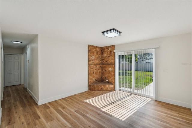 spare room featuring brick wall, a healthy amount of sunlight, and hardwood / wood-style flooring