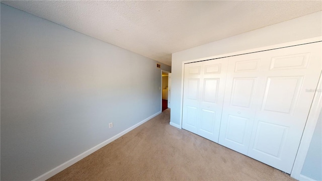 unfurnished bedroom with a textured ceiling, a closet, and light colored carpet