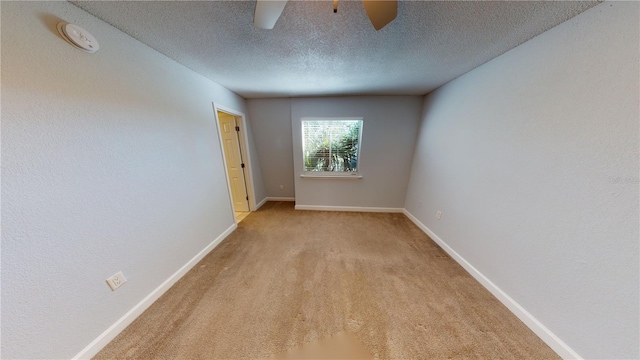 carpeted spare room with a ceiling fan, baseboards, and a textured ceiling