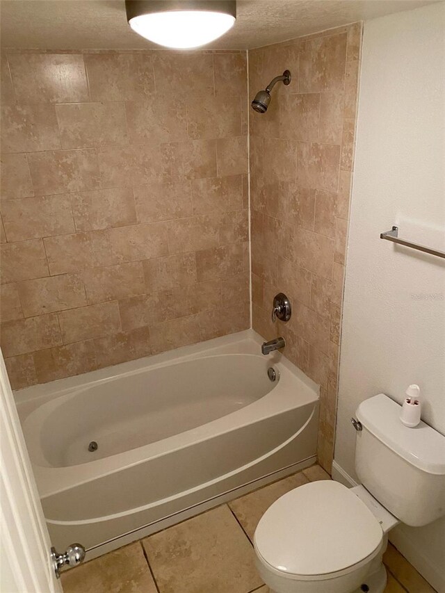 bathroom featuring tiled shower / bath combo, toilet, a textured ceiling, and tile patterned flooring