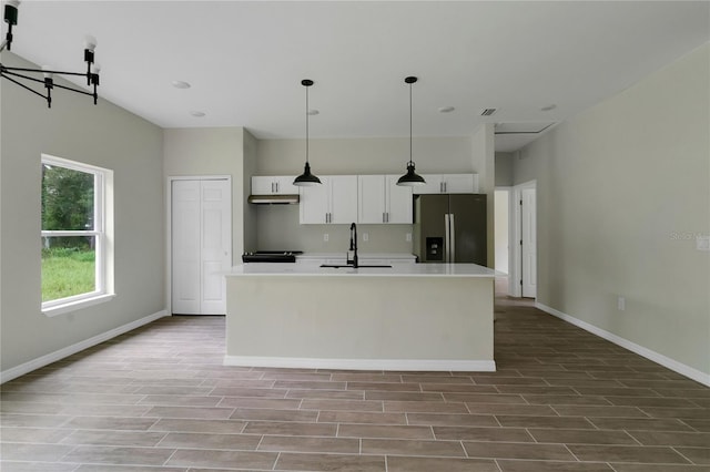 kitchen featuring pendant lighting, a kitchen island with sink, white cabinetry, sink, and stainless steel fridge