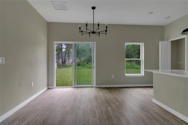 unfurnished dining area with hardwood / wood-style floors, a notable chandelier, and a healthy amount of sunlight