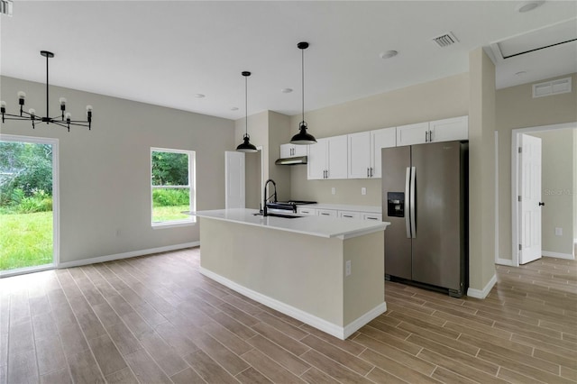 kitchen featuring a chandelier, a kitchen island with sink, white cabinetry, decorative light fixtures, and stainless steel fridge