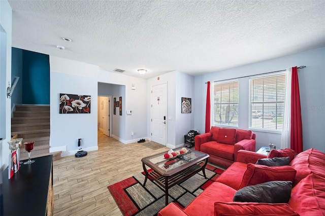 living area featuring visible vents, baseboards, light wood-style flooring, stairs, and a textured ceiling