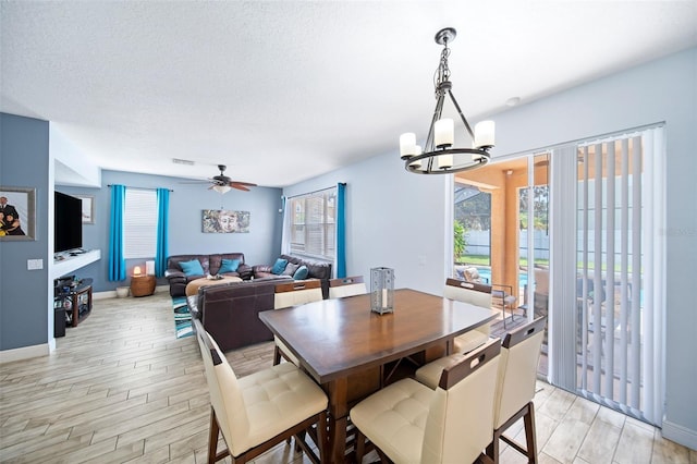 dining space with ceiling fan with notable chandelier, light wood-type flooring, and a textured ceiling