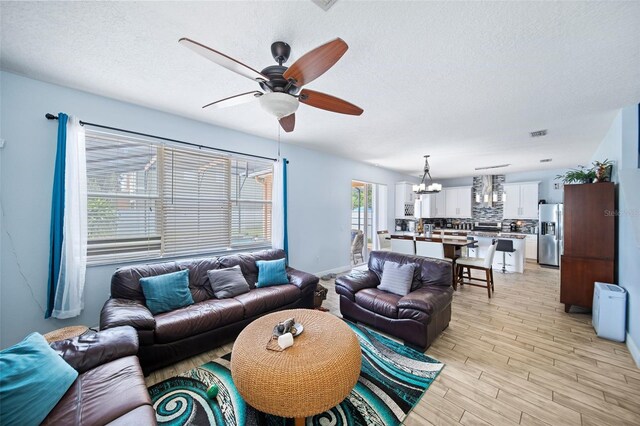 living room featuring a textured ceiling, ceiling fan with notable chandelier, and light hardwood / wood-style floors