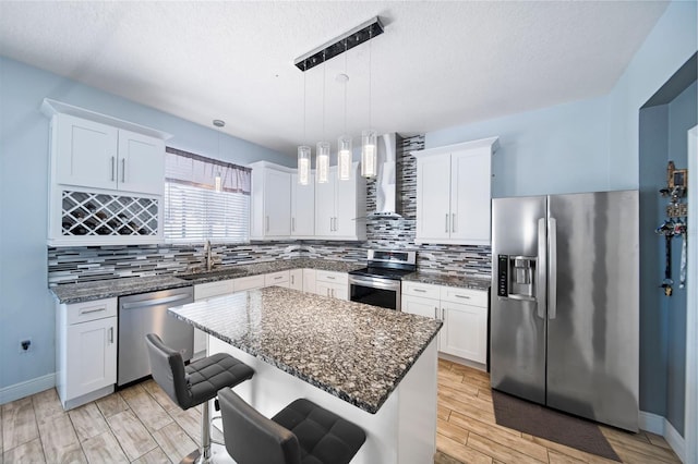 kitchen featuring sink, hanging light fixtures, a kitchen island, wall chimney exhaust hood, and appliances with stainless steel finishes