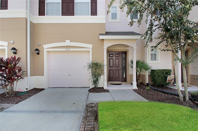 view of exterior entry featuring driveway, an attached garage, roof with shingles, and stucco siding