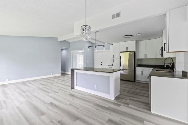 kitchen featuring stainless steel fridge, sink, pendant lighting, a chandelier, and white cabinetry