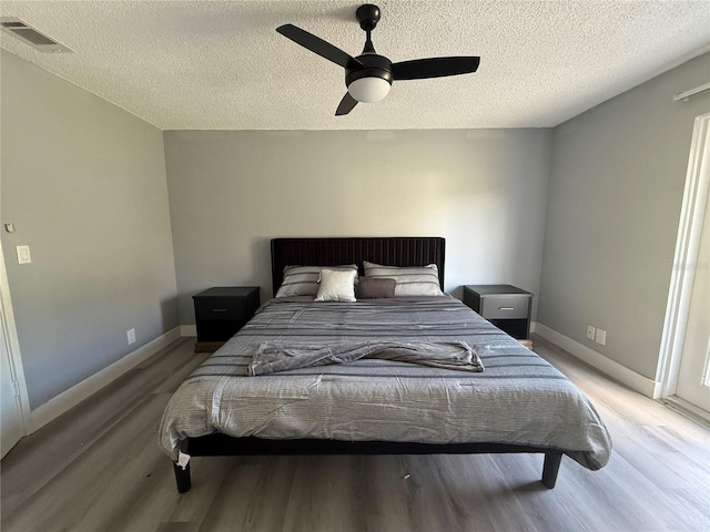 bedroom with ceiling fan, wood-type flooring, and a textured ceiling