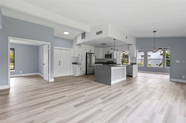 kitchen featuring appliances with stainless steel finishes, a kitchen island, vaulted ceiling with beams, white cabinetry, and hanging light fixtures