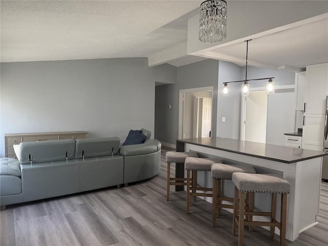 kitchen featuring a kitchen breakfast bar, pendant lighting, an inviting chandelier, white cabinets, and vaulted ceiling with beams