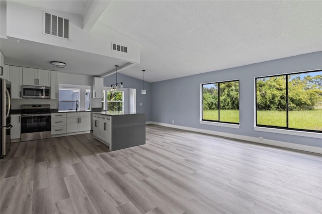 kitchen with appliances with stainless steel finishes, lofted ceiling with beams, decorative light fixtures, light hardwood / wood-style floors, and white cabinetry