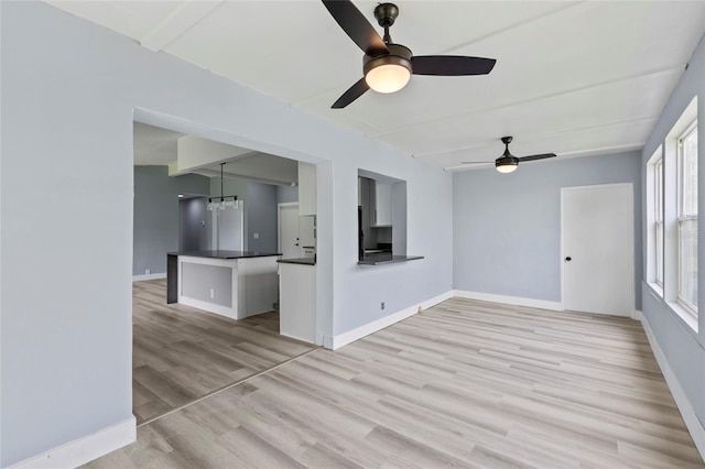 unfurnished living room with ceiling fan with notable chandelier and light wood-type flooring