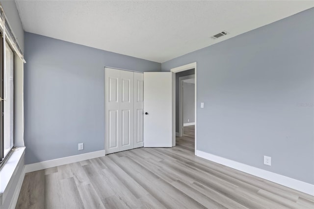 unfurnished bedroom with a textured ceiling, light hardwood / wood-style flooring, and a closet