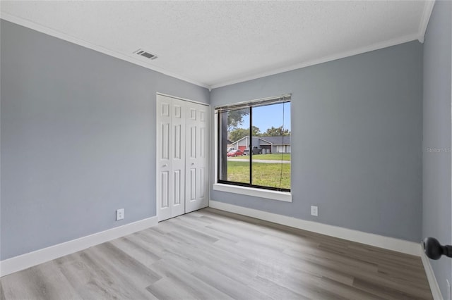 spare room with light wood-type flooring, a textured ceiling, and ornamental molding