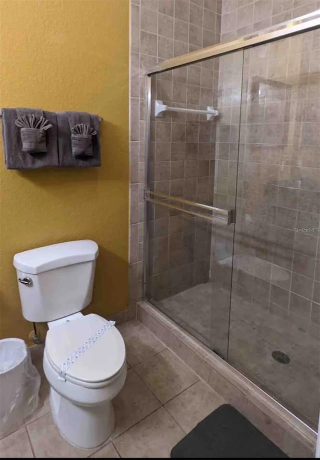 bathroom with tile patterned floors, toilet, and an enclosed shower