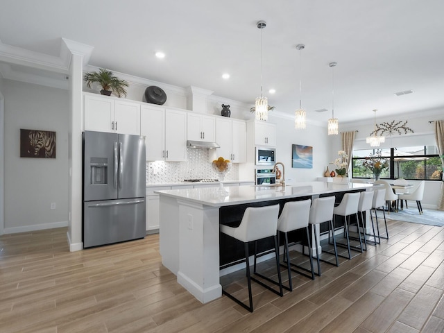 kitchen featuring stainless steel appliances, an island with sink, light hardwood / wood-style flooring, white cabinets, and pendant lighting