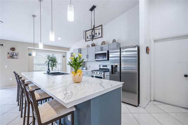 kitchen with lofted ceiling, sink, a kitchen island with sink, stainless steel appliances, and decorative light fixtures