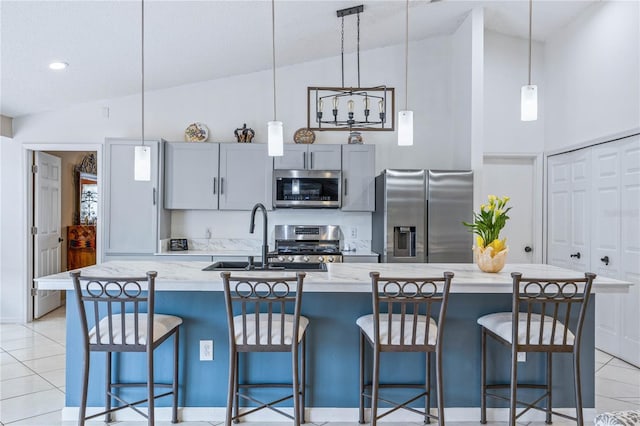 kitchen with light stone counters, a breakfast bar, decorative light fixtures, a kitchen island with sink, and stainless steel appliances