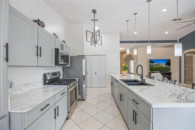 kitchen with arched walkways, a sink, hanging light fixtures, appliances with stainless steel finishes, and an island with sink