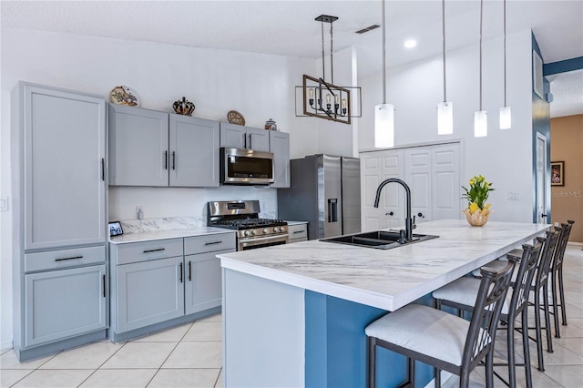 kitchen with a sink, hanging light fixtures, appliances with stainless steel finishes, a kitchen bar, and a center island with sink