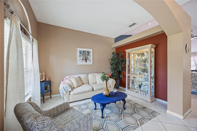 living area with light tile patterned floors, arched walkways, visible vents, and baseboards