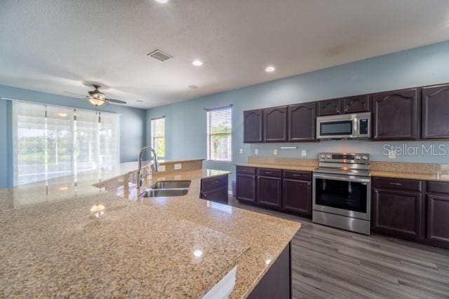 kitchen with light stone countertops, sink, stainless steel appliances, dark hardwood / wood-style floors, and dark brown cabinets