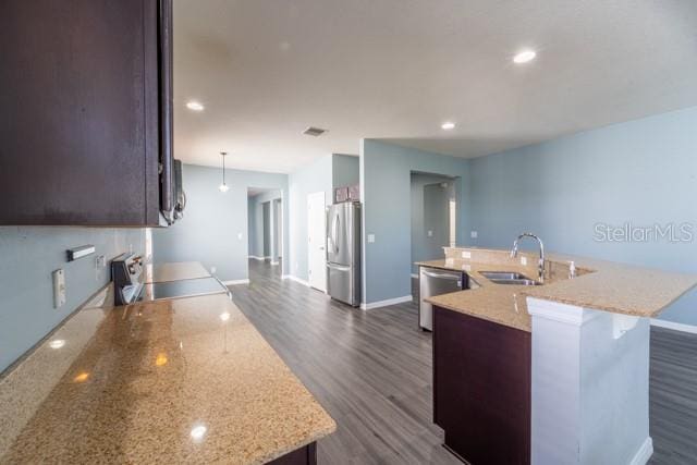 kitchen featuring light stone counters, stainless steel appliances, dark wood-type flooring, sink, and a center island with sink