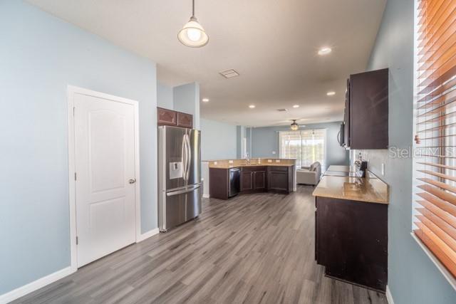 kitchen with dark brown cabinets, stainless steel appliances, ceiling fan, hardwood / wood-style flooring, and hanging light fixtures