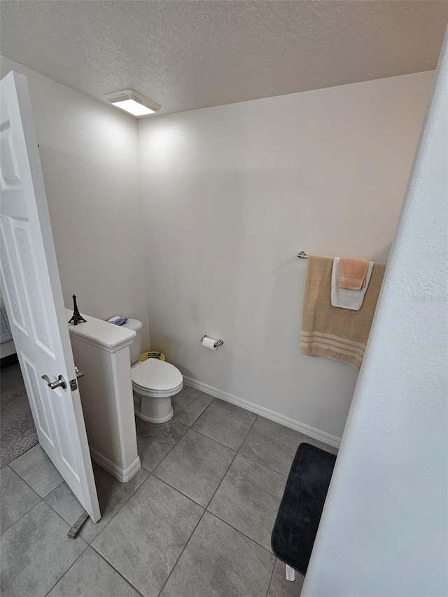 bathroom with toilet, a textured ceiling, and tile patterned floors