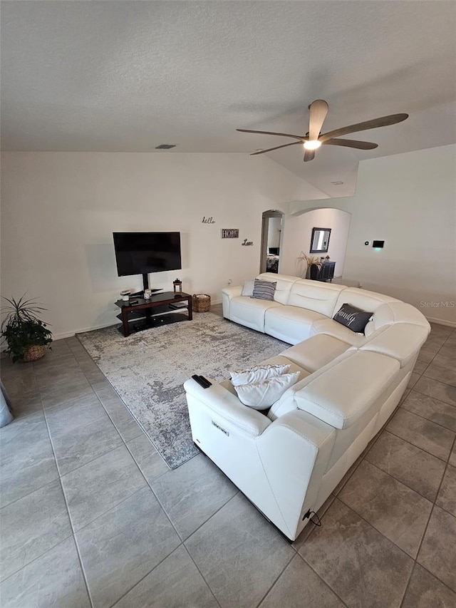 unfurnished living room featuring ceiling fan, vaulted ceiling, a textured ceiling, and tile patterned floors