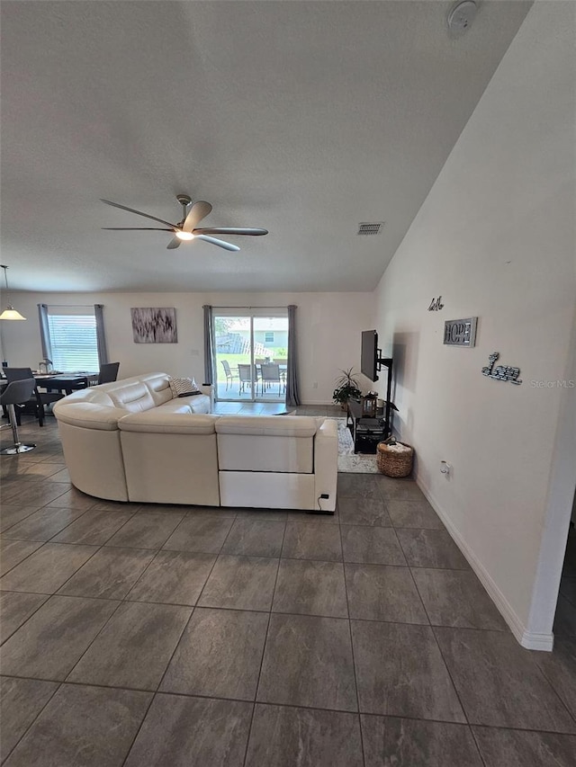 living room with ceiling fan, dark tile patterned flooring, and vaulted ceiling