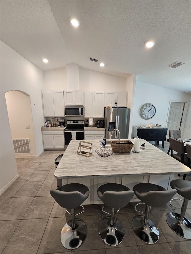 kitchen featuring appliances with stainless steel finishes, vaulted ceiling, a kitchen bar, and white cabinets