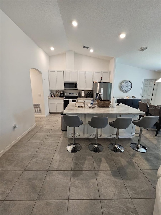 kitchen with appliances with stainless steel finishes, high vaulted ceiling, a center island with sink, and white cabinets