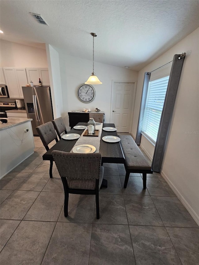 tiled dining room with vaulted ceiling and a textured ceiling